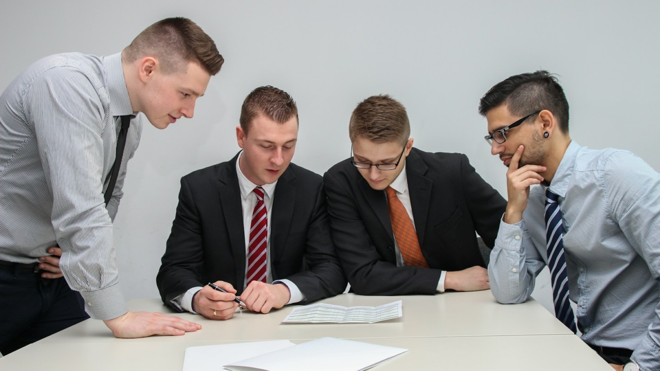 four men looking to the paper on table